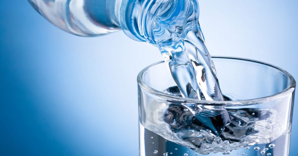 Pouring water from bottle into glass on blue background