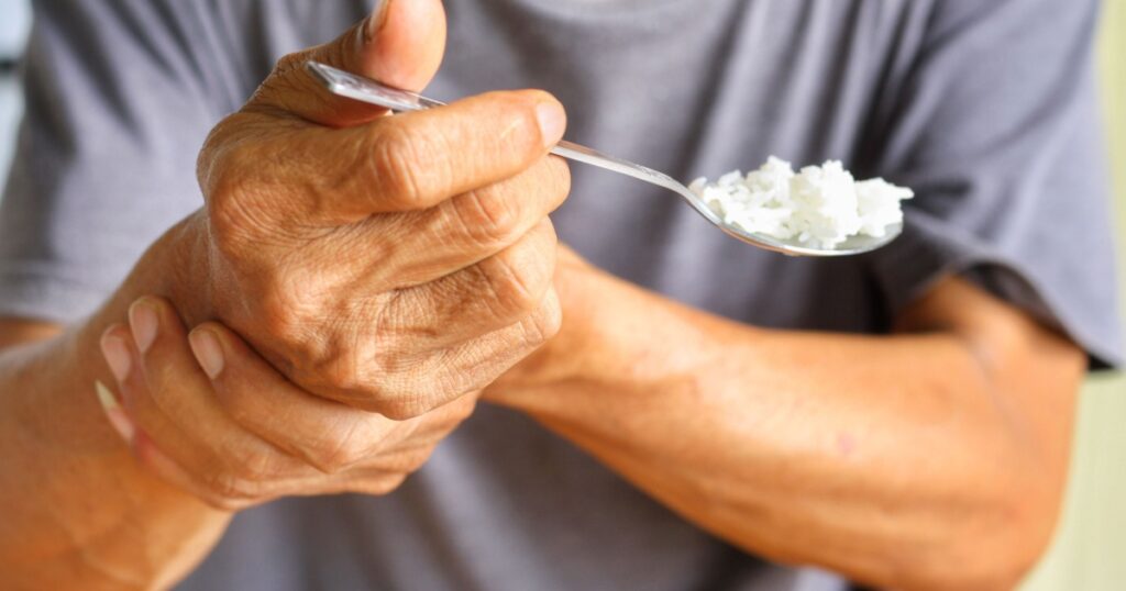 Elderly man is holding his hand while eating because Parkinson's disease.Tremor is most symptom and make a trouble for doing activities such as eat.Health care or elderly concept.Selective focus.
