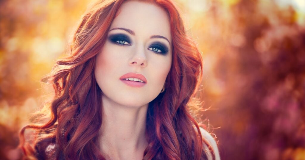 Outdoors portrait of beautiful woman with red hair and smoky eyes makeup