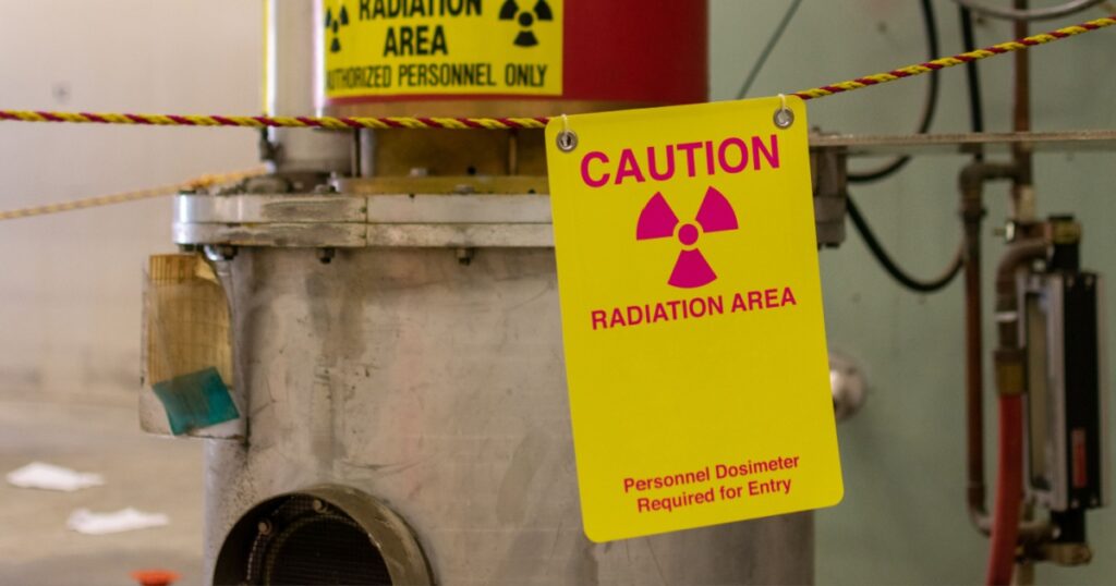 Ionizing radiation hazard symbol, caution radiation area and personnel dosimeter required text on yellow warning sign displayed on the equipment that produces dangerous ionizing radiation