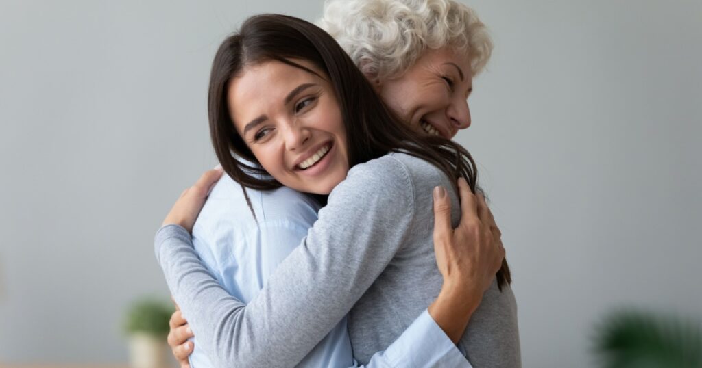 Happy young lady adult daughter granddaughter visiting embracing hugging old senior retired grandmother cuddling bonding, two age generations women expressing love and care at reunion meeting at home