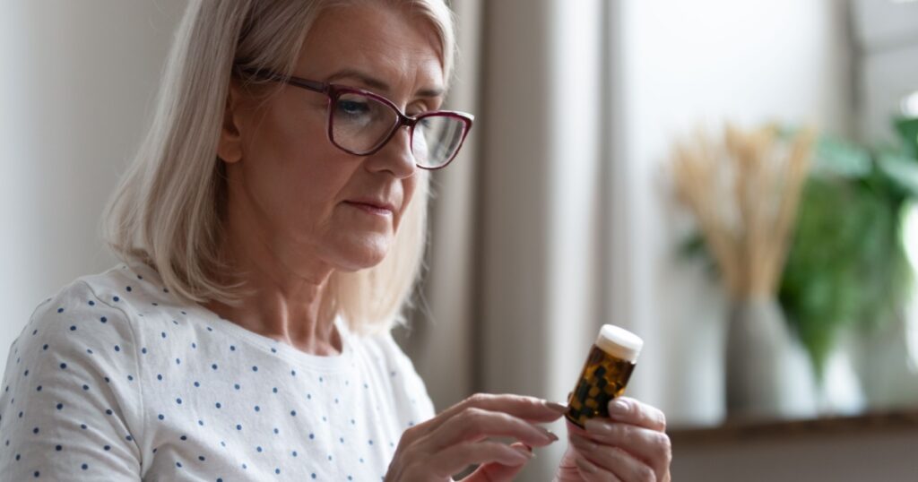 Mature woman in glasses hold bottle with pills read medicine instruction on packaging before take meds, senior female retiree in spectacles thinking of medication treatment, elderly healthcare concept
