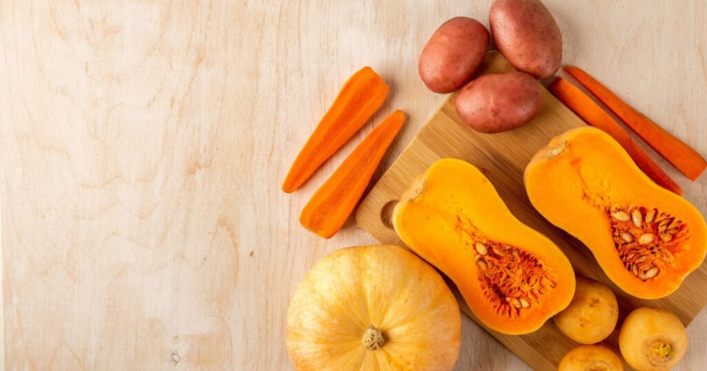 two pieces of sliced pumpkin and carrot, round pumpkin, potato, turnip and garlic are laid out on a bamboo cutting Board and a light wooden background, top view, space for text, flat lay food