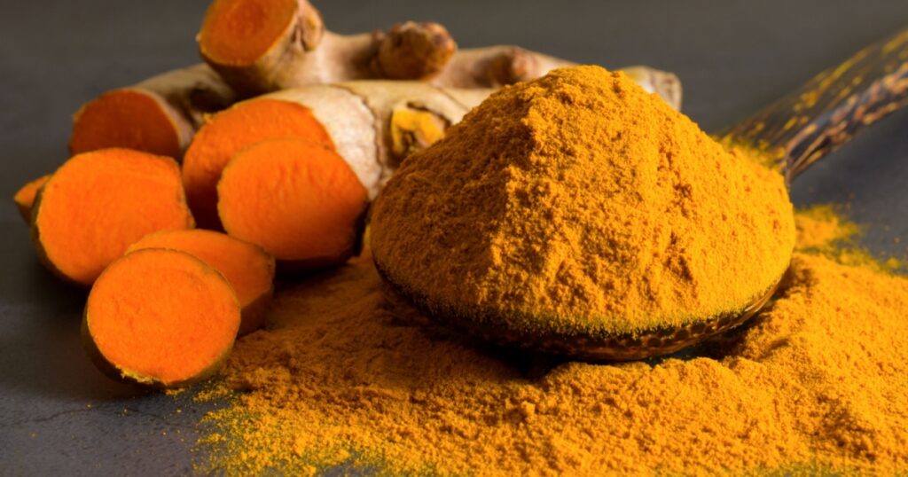 Turmeric (curcumin) powder in a wooden ladle and fresh rhizome on a black background,For spices and medicine.