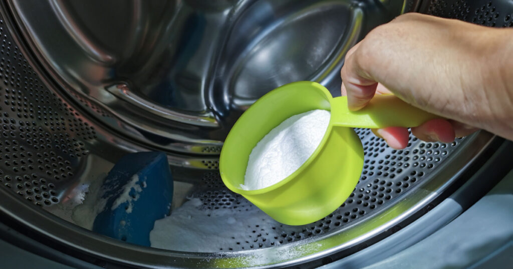 Close up hand adding baking soda powder in to front-loading washing machine for clean inside the washer drum.