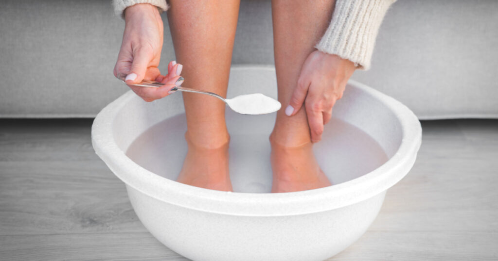 Woman put spoon of baking soda in bath with hot water for her feet. Homemade bath soak for dry feet skin.
