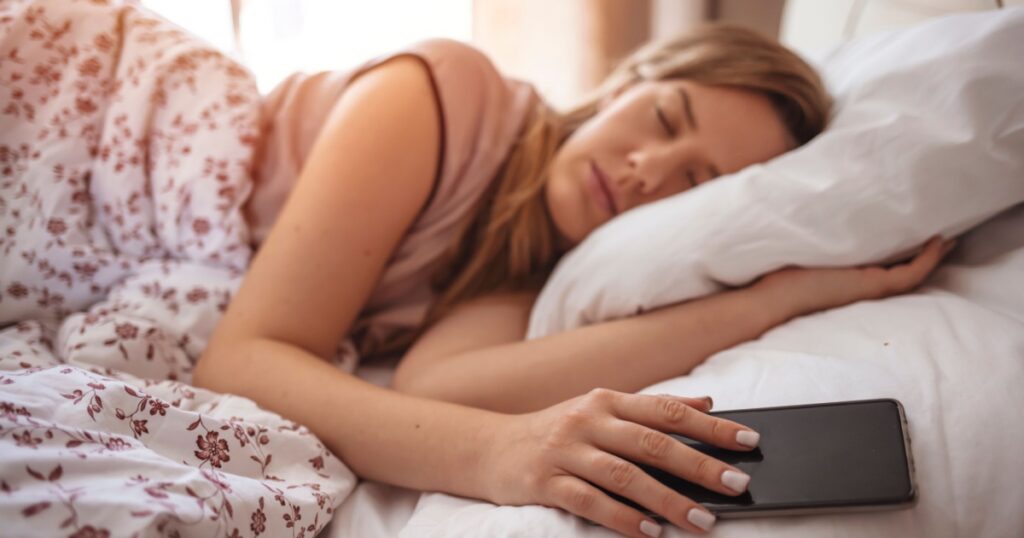 Woman alseep next to smart phone. Woman sleeping in bed being woken by mobile phone. Woman sleeping in bed and holding a mobile phone. Young girl sleep in bed still holding on her mobile phone
