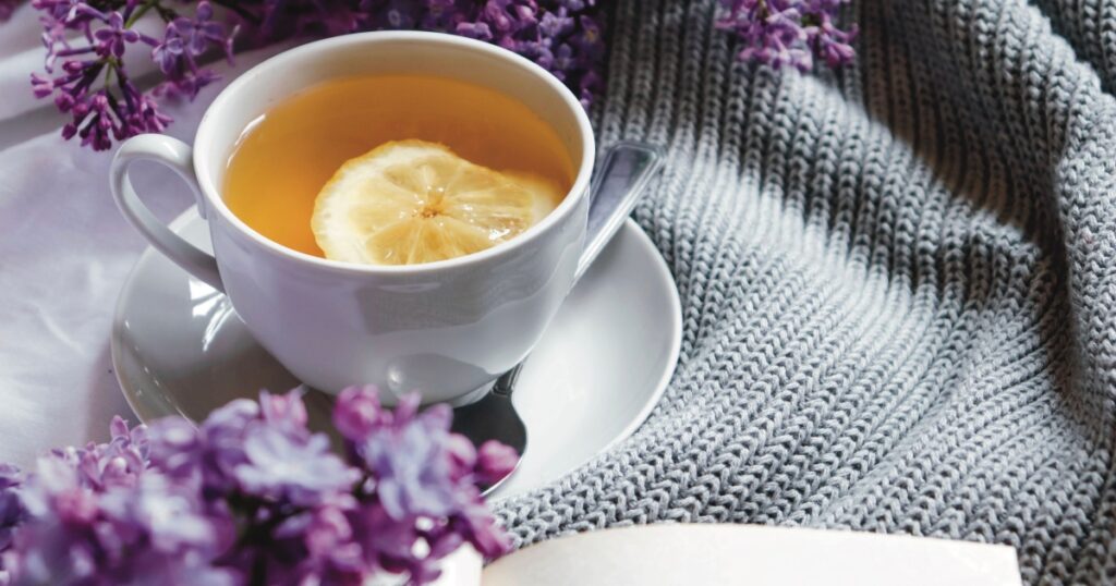 Spring composition flat lay with white cup of lemon tea, beautiful bouquet of lilacs, sweater. Concept of spring and comfort. Still life spring photography for card, poster, banner, wallpaper.