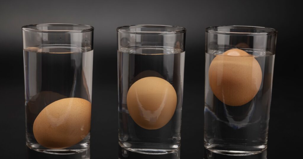 Eggs in water test on transparent glass , Egg freshness test on black background , Bad egg floats in water