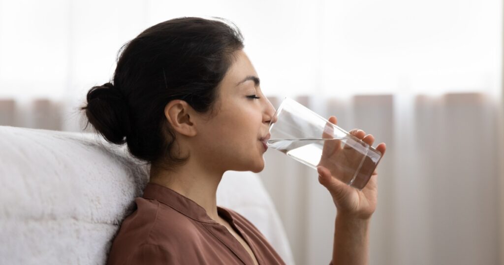 Drinking water. Side view young indian woman enjoy pure fresh cool mineral water at morning. Profile shot of thirsty millennial mixed race lady hold glass swallow crystal still aqua with closed eyes