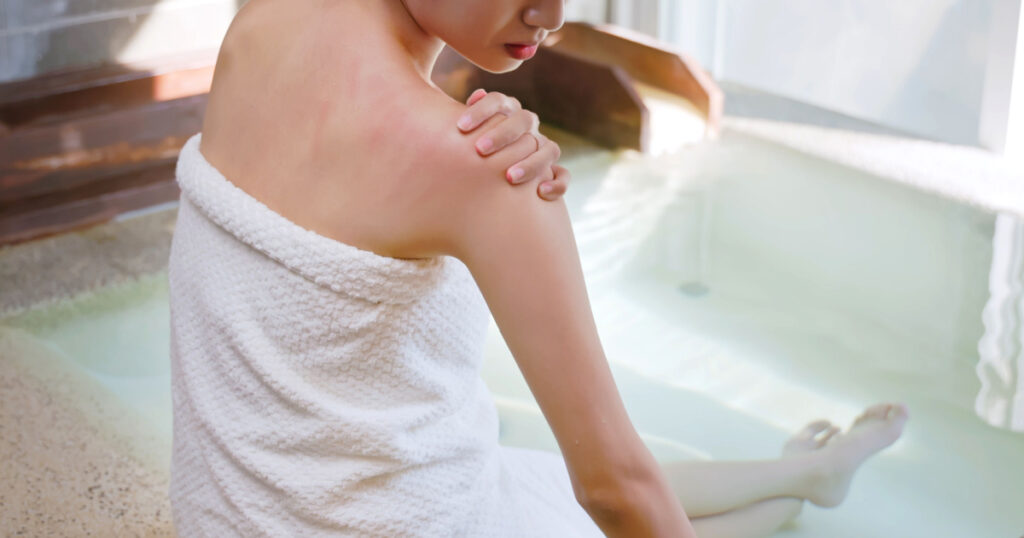 asian young woman has dry skin and scratches her shoulder while she sitting in hot spring