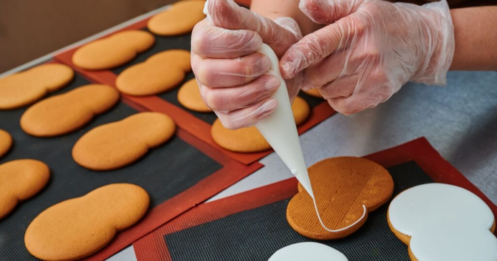 applying a layer of glaze to a confectionery product using a pastry bag. A row of gingerbread cookies on the kitchen table. Confectioner's inventory. Product surface decoration