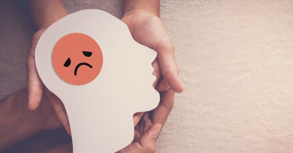Adult and child hands holding sad face in brain paper cutout, unhappy hormones, imbalance brain chemicals, negative mental health concept