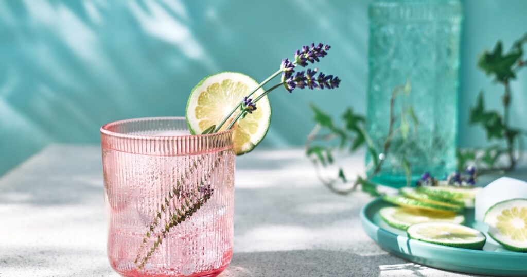 Cool lavender lemonade with lime slices and lavender flower on the table near pastel light blue background. Healthy organic summer soda drink. Detox water. Diet unalcolic coctail.
