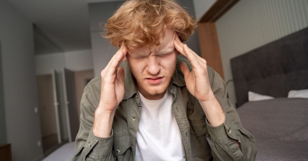 Stressed young ginger man suffering from terrible strong headache or migraine closeup shot. Tired upset millennial irish redhead guy feeling pain touching aching head massaging temples