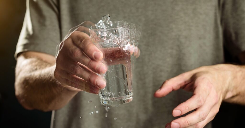 A man holds a glass of water with a shaking hand. The concept of parkinson's disease and tremor.