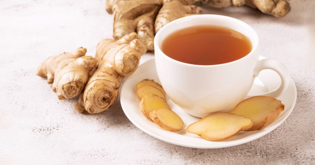 Cup of hot ginger tea with ginger root and slices on gray background.