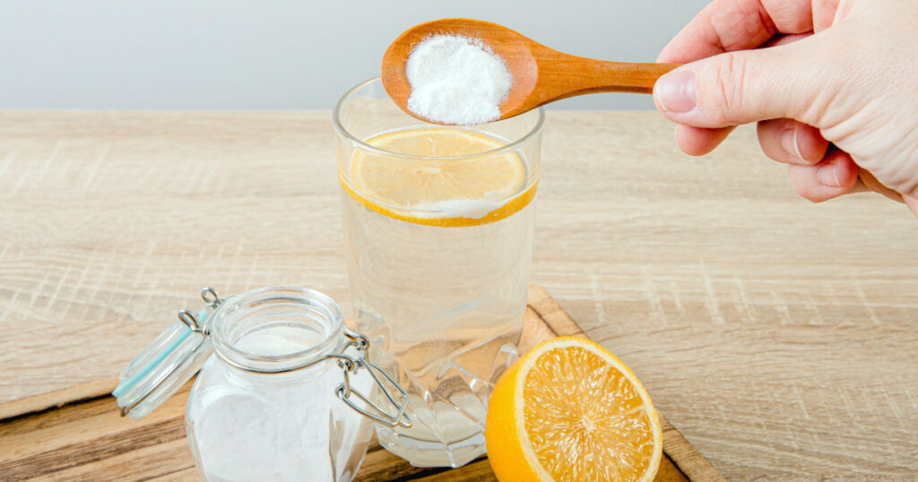 Close up of woman hand pouring baking soda in drinking glass with water and lemon juice, health benefits for digestive system concept.