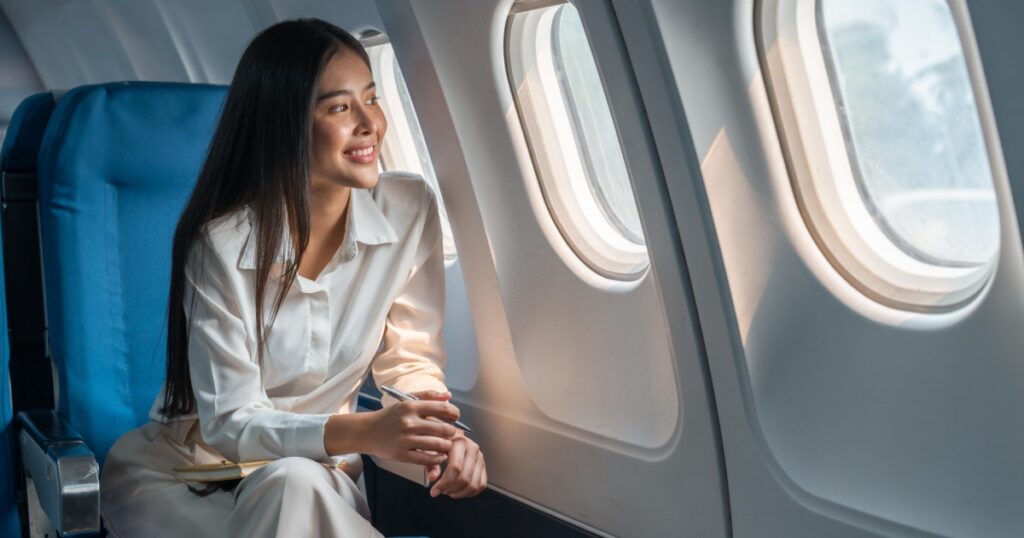 Asian woman sitting in a seat in airplane and looking out the window going on a trip vacation travel concept