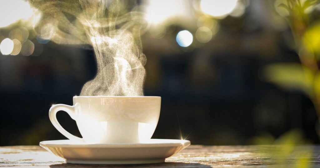 Concept Coffee Cup, Mug, hot drink, espresso, breakfast. close-up natural steam smoke of coffee from hot coffee cup on old wooden table in morning warm sunlight flare, outdoor background