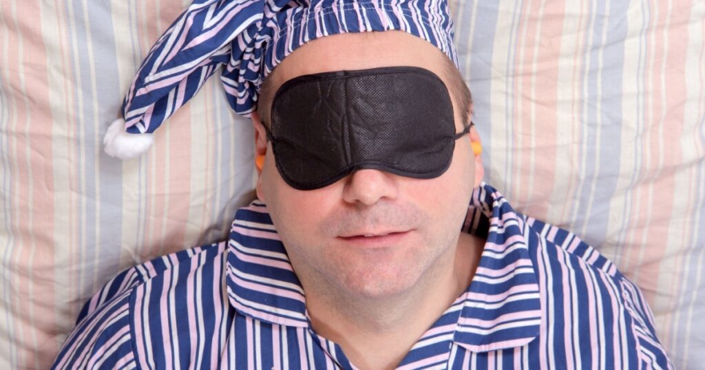 Man sleeping with a mask on eyes. Portrait of man in pajamas sleeping on his back in bed. Sleeper with a night cap sleeps with a drape eyes.