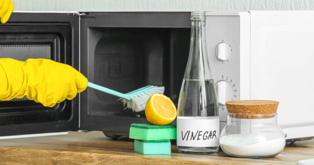 Woman cleaning microwave oven with brush, baking, soda and vinegar at home