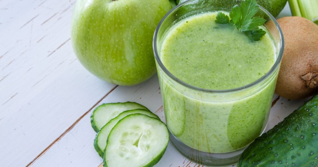 Green smoothie and ingredients - avocado, apple, celery, cucumber, broccoli, kiwi, dill, parsley, white wood background