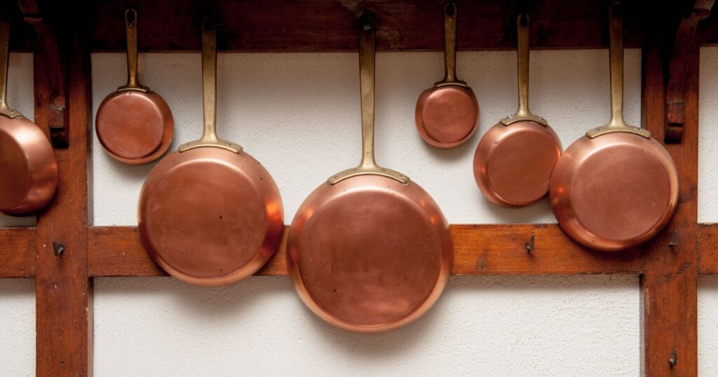 Row of vintage copper pans, different size, hung on wooden shelf in kitchen, vertical frame