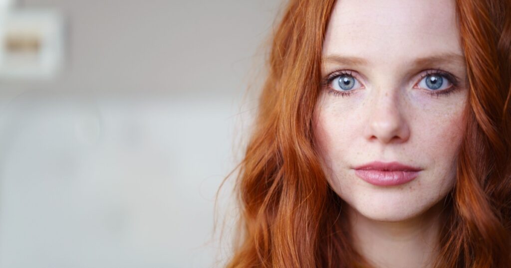 Gorgeous young redhead woman with long coppery hair and blue eyes looking at the camera, close up head shot with copy space