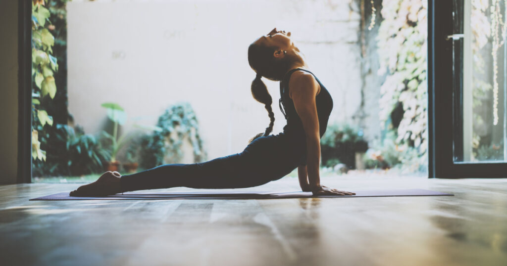 Portrait of gorgeous young woman practicing yoga indoor. Beautiful girl practice cobra asana in class.Calmness and relax, female happiness.Horizontal, blurred background