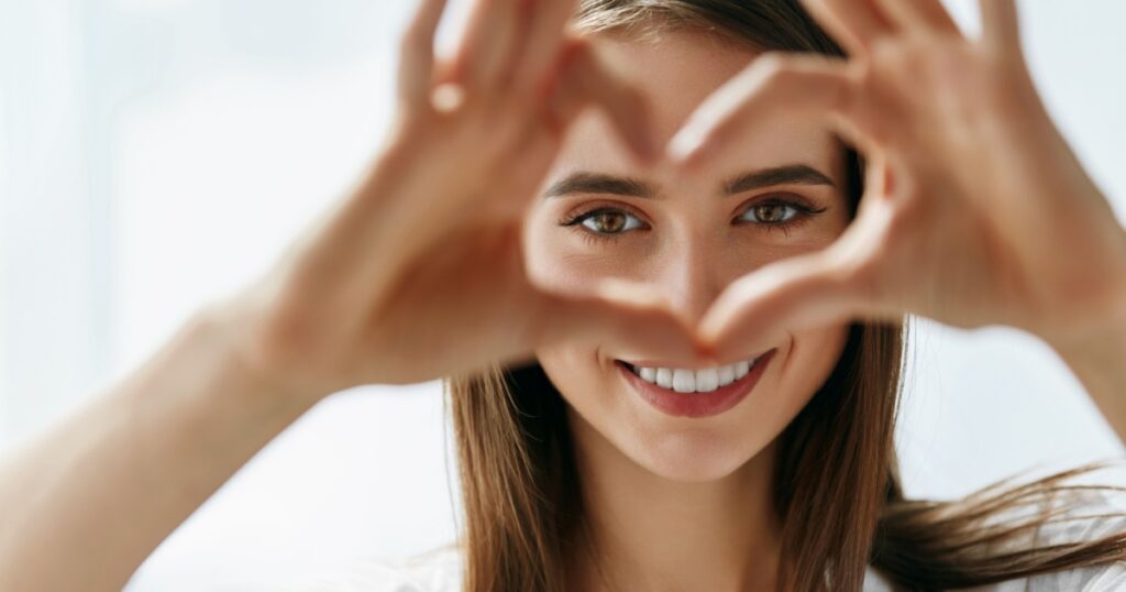 Healthy Eyes And Vision. Portrait Of Beautiful Happy Woman Holding Heart Shaped Hands Near Eyes. Closeup Of Smiling Girl With Healthy Skin Showing Love Sign. Eyecare. High Resolution Image