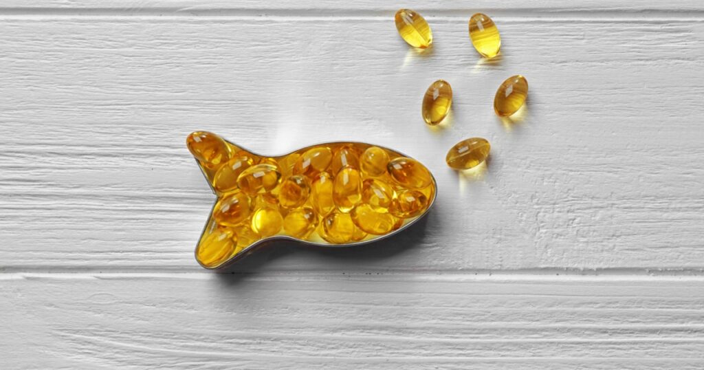 Capsules of cod liver oil arranged in a fish shape on white wooden background