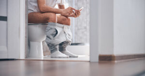 Your Stool Shape Could Be a Symptom of Colon Cancer, Doctors Warn person sitting on toilet
