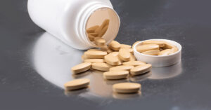 7 Supplements That Could Be Causing More Harm Than Good pill bottle containing brown supplement tablets spilled onto metallic surface