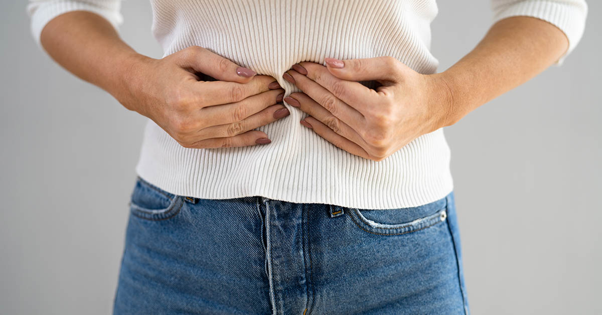 woman with hands placed over abdomen. diverticulitis symptoms concept