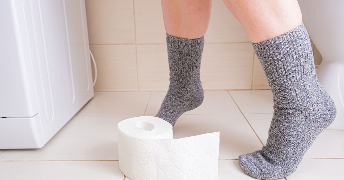 person on toilet. Toilet paper on bathroom floor at their feet