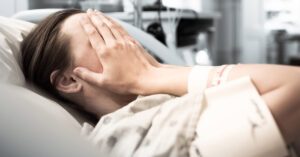 Woman Disabled From Fluoroquinolone Toxicity After Use of Common Antibiotic woman with hands placed over face laying in hospital bed
