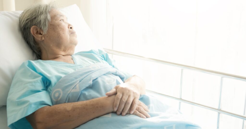 Elderly patient alone in bed. Alone and stress, missing her grand children. Looking at window. Very senior, old chinese woman.