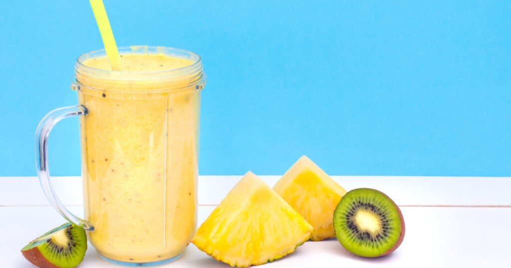 Fresh tropical smoothie and slices of kiwi and pineapple on a turquoise background