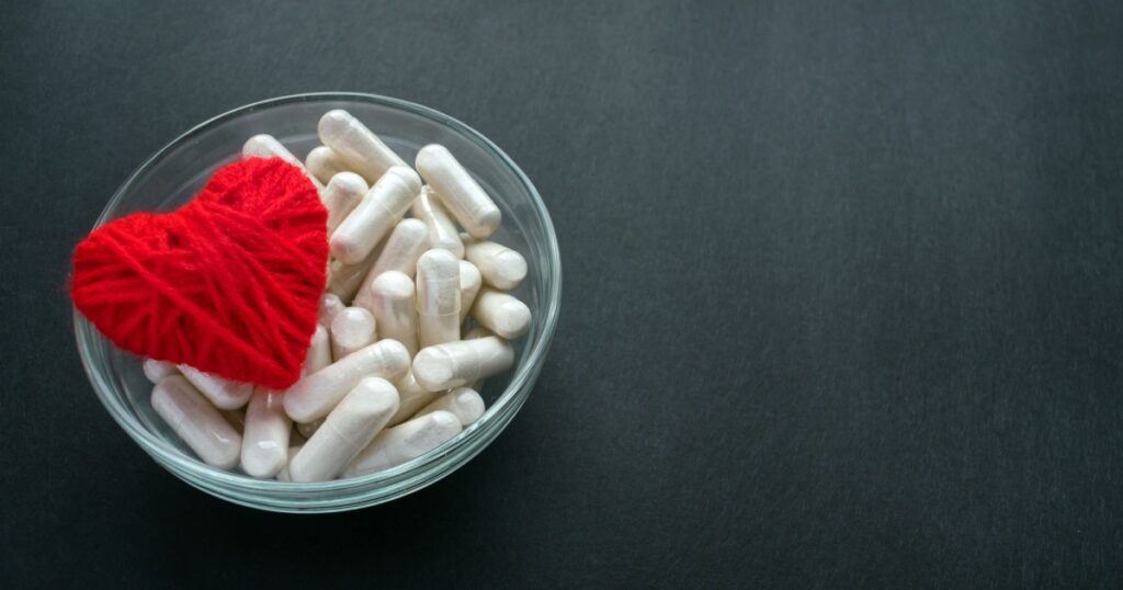 White veg capsules and red thread heart in glass bowl on black background. Anticoagulant, Blood Thinners. Cardiac Medications, pills for the heart. Treat Heart disease Failure