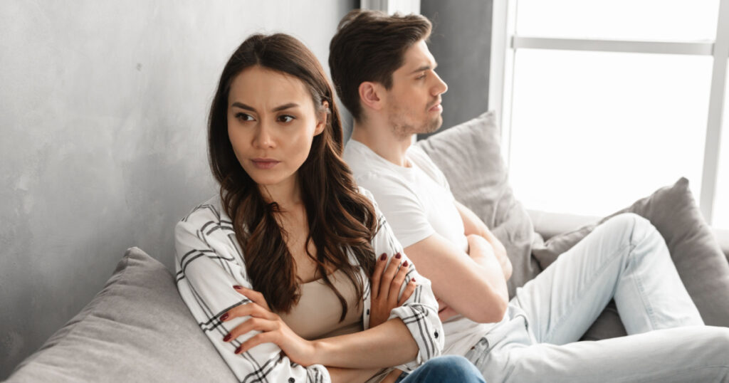 Photo of resentful guy and girl acting like arguing couple and not speaking to each other, while sitting together on couch at home isolated over white background