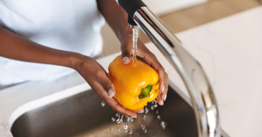 Close up of a afro american woman washing capsicum to make a salad at the kitchen
