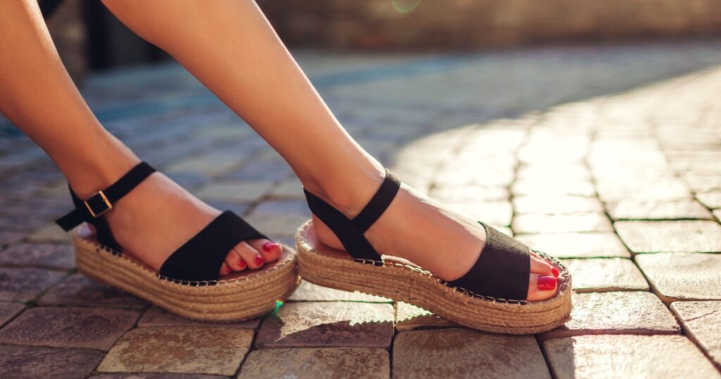 Stylish woman wearing black summer shoes with straw sole outdoors. Comfortable sandals. Beauty fashion.