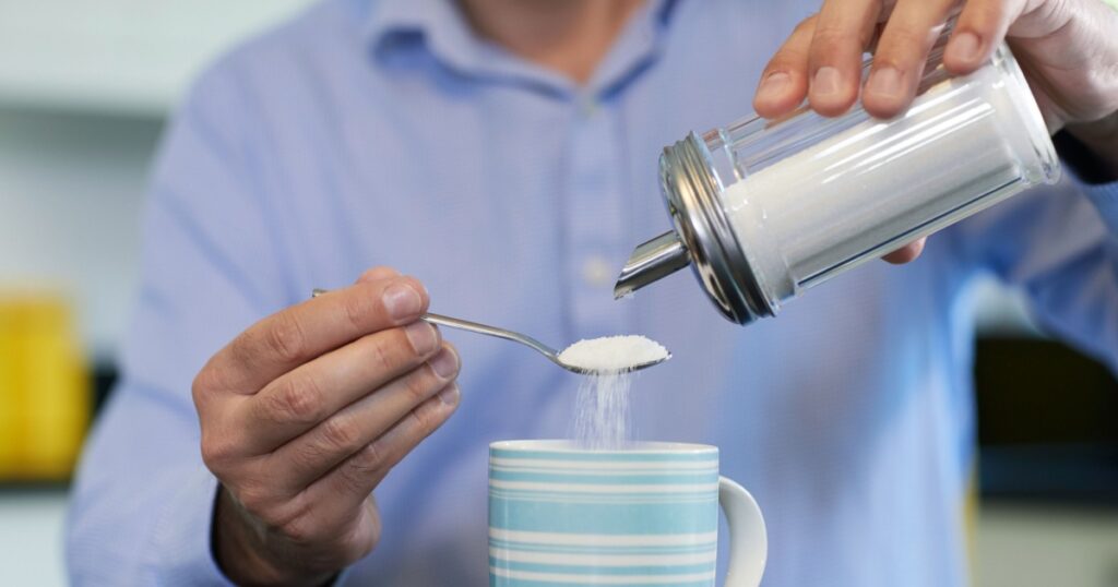 Close Up Of Mature Man Adding Sugar To Hot Drink At Home