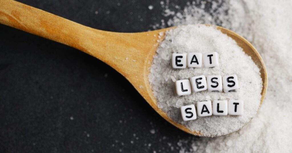 Eat less salt advice written with plastic letter beads on granulated salt – healthy food lifestyle