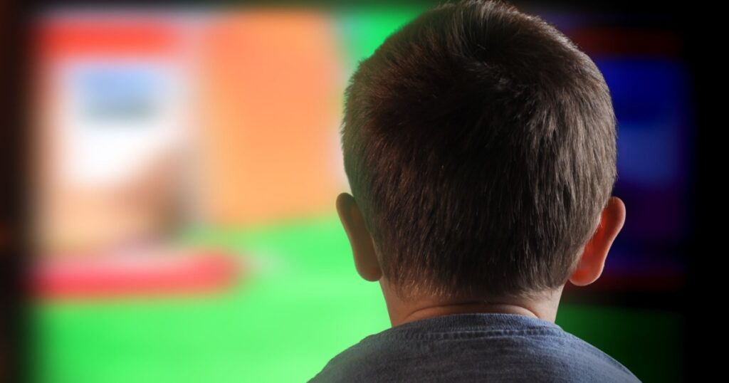 A young boy is watching a television screen with his back for a tv effect on children or a communication concept.