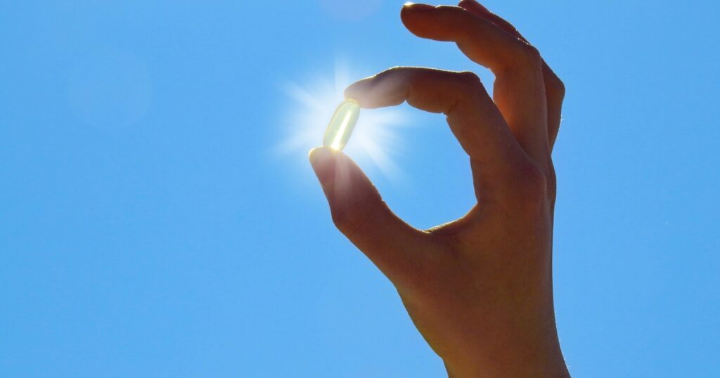Young Woman is holding Vitamin D Capsule. Sun and blue Sky.