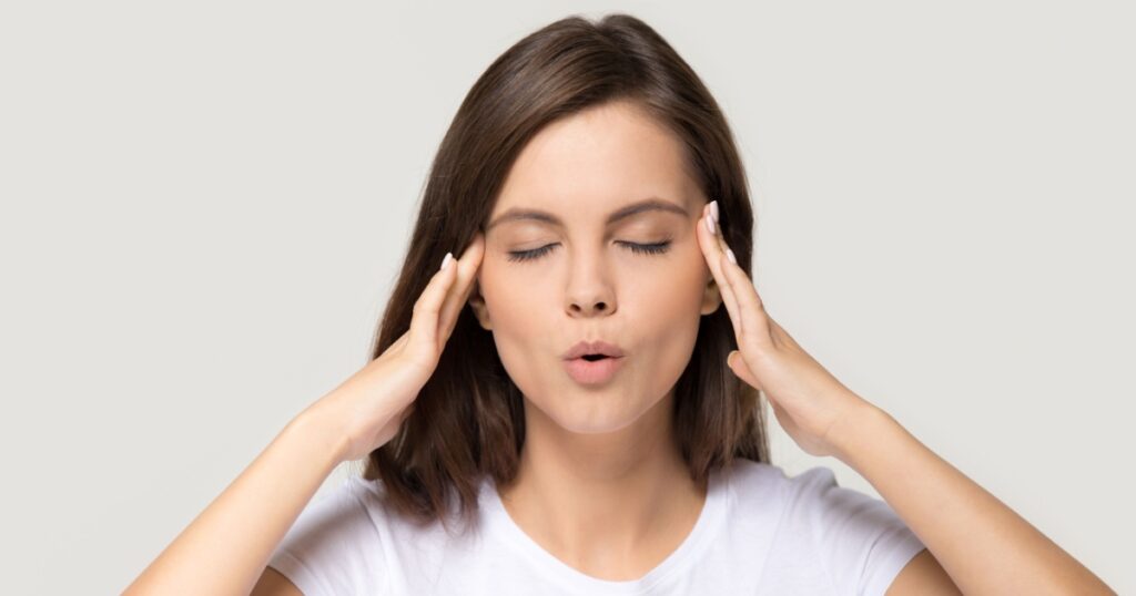 Stressed teen girl calming down relieving headache emotional stress relief, nervous young woman meditating massaging temples doing breathing exercises isolated on white grey studio