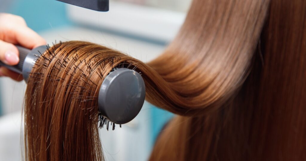 Drying long shine brown hair with dryer and round brush. Beauty shop.
