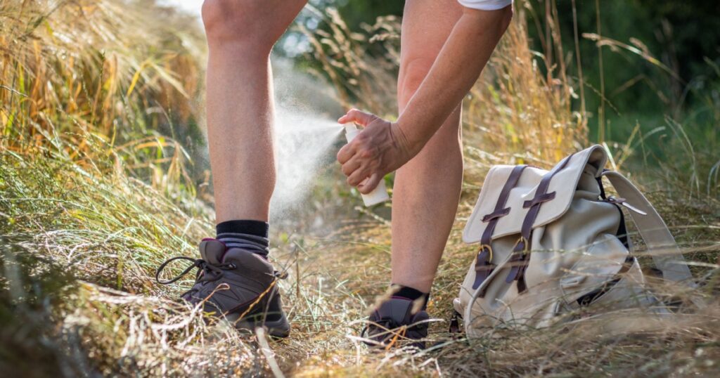 Woman tourist spraying insect repellent against tick and mosquito in nature. Applying skin protection on leg